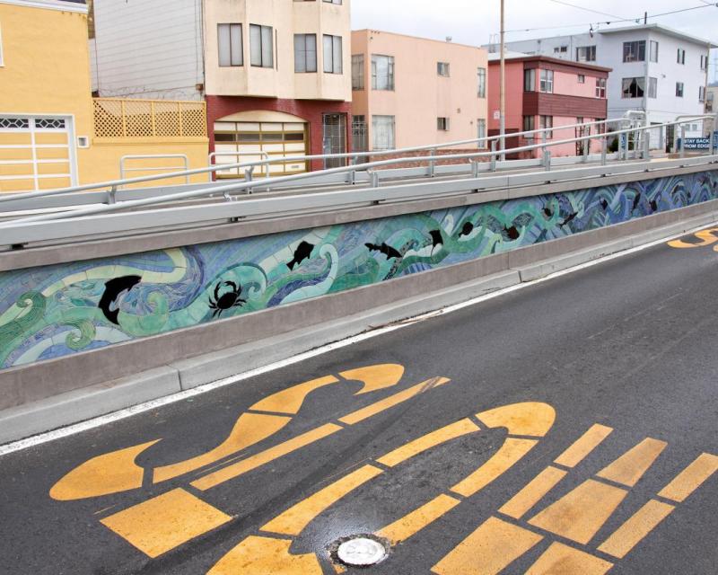 We see artwork on a new L Taraval accessible boarding platform with a freshly paved road beside it and the word "slow."