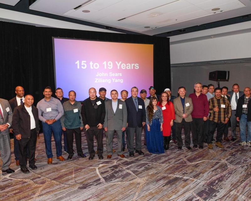 Safe Driver Award winners smile at the 2024 dinner celebrating their work. A crowd poses in front of a projector that says "15 t