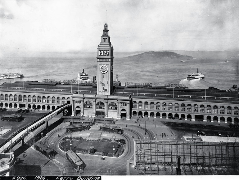 In 1928, the Ferry Building dominates a view of the Bay adjacent Embarcadero with a loop for Market streetcars, a walkway for pedestrians and several ferries approaching from the San Francisco Bay.