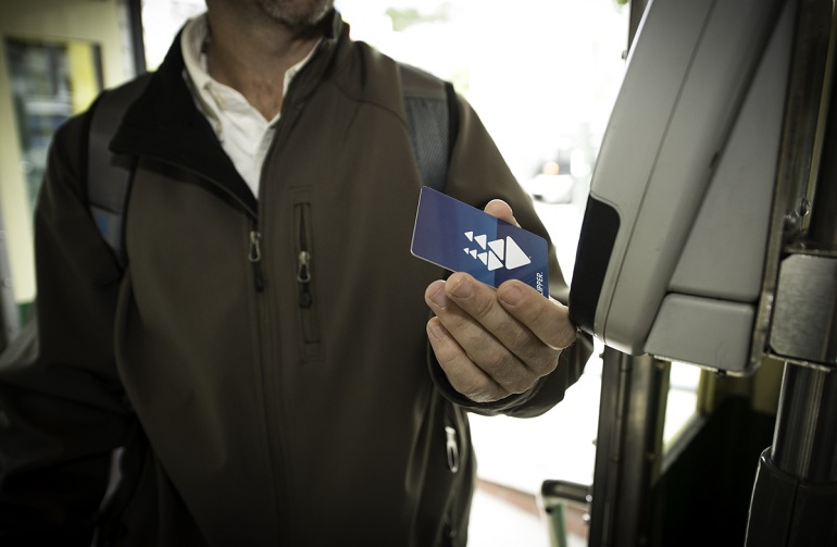 A man entering a Muni vehicle holds a Clipper Card in front of a digital card reader.