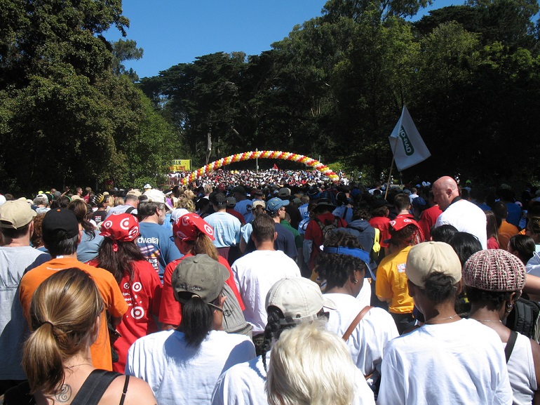 Thousands of people together in the park surrounded by trees under a bright blue sky.