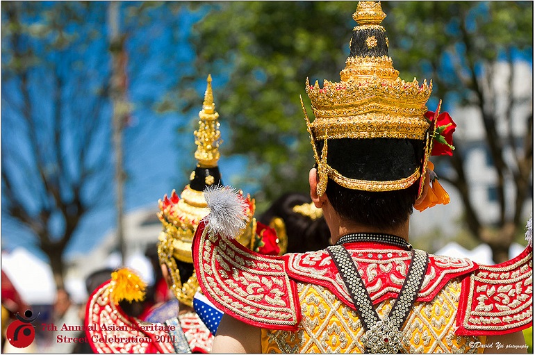 A person in a ceremonial gold, red and white Thai attire on a Sunday day.