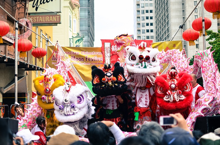 Colorful and ornate costumed Chinese lion dancers perform in front of a crowd during the afternoon