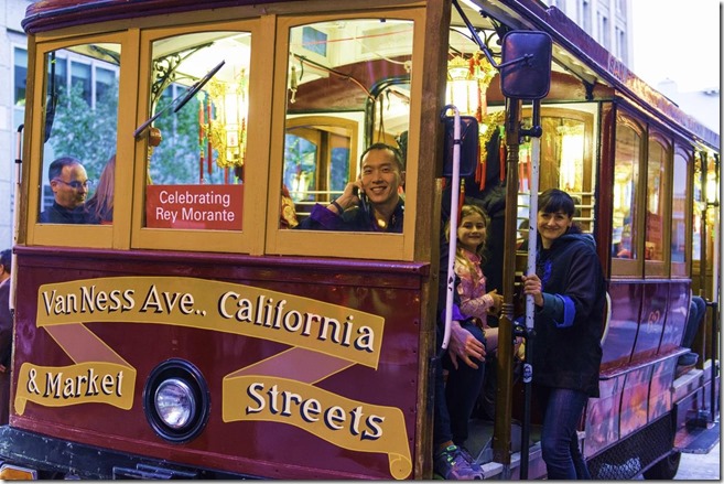 SFMTA staff members ride on the front of the motorized cable car which features a sign that says, "Celebrating Rey Morante."