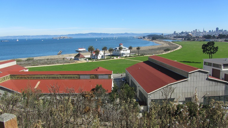 A panoramic view of Chrissy Field under a bright blu sky with blue bay water in the background.