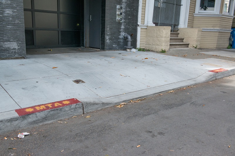 A driveway with short red curb zones on either side and an "MTA" stencil marking.