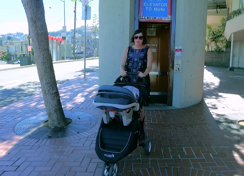 A woman with a stroller exits a Muni elevator on the street above Castro Station.