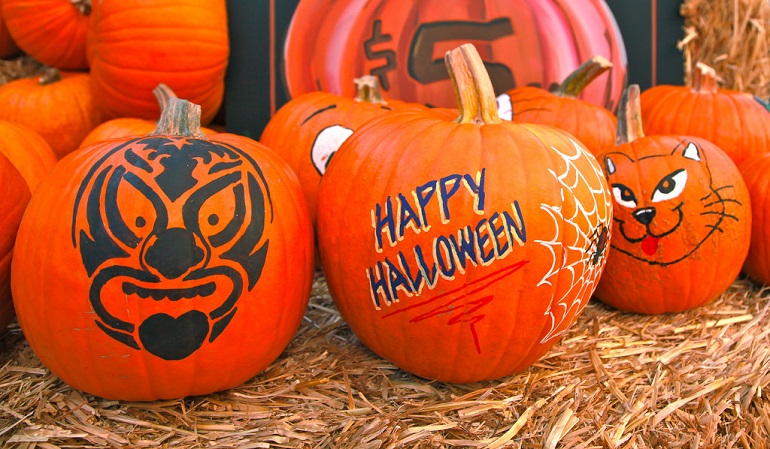 Three bright orange pumpkins decorated for Halloween on a hay stack.