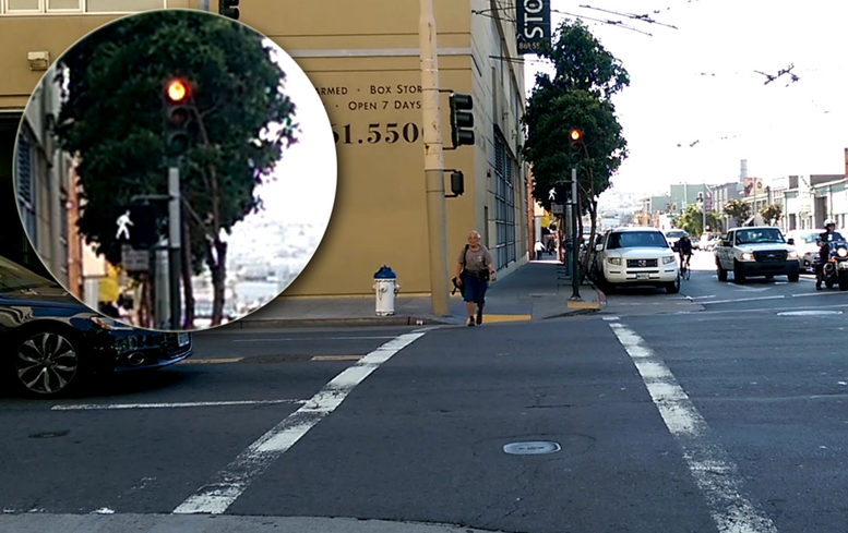 A woman enters a crosswalk with a "walk" signal showing behind her, while a signal for vehicle traffic above displays red.