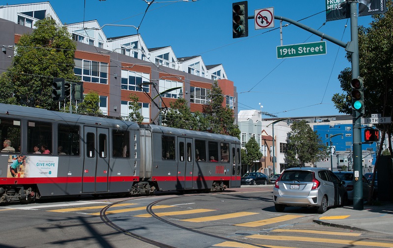 A Muni train on the T Third Line travels down Third Street next to a track spur that turns down 19th Street.