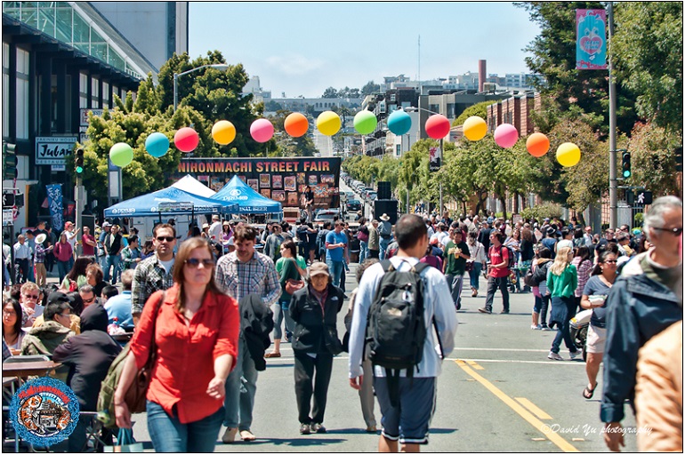 People out enjoying a street fair under a bright afternoon sky.