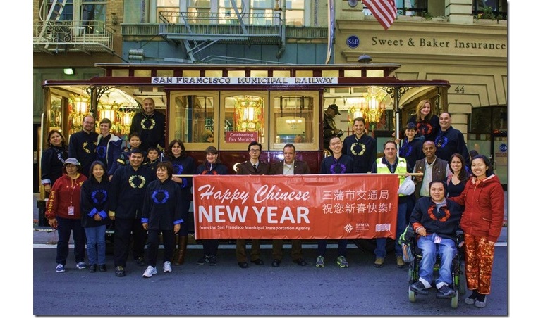 A couple dozen members of the SFMTA contingent stand in front of the agency’s motorized cable car holding a banner that says "Happy Chinese New Year."