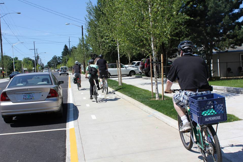 People bike on a raised, parking-protected bike lane in Portland, Oregon.