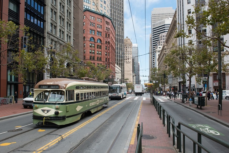 A Muni historic streetcar, trolley bus and other vehicles travel on Market Street at 3rd Street.