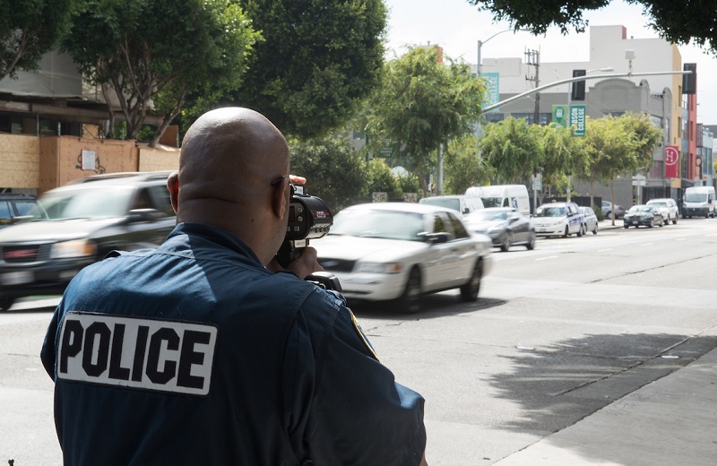 An SFPD officer points a LIDAR device at passing vehicles to measure speeds on Folsom Street.