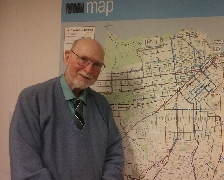 John Moore stands with a smile in front of a Muni Map.