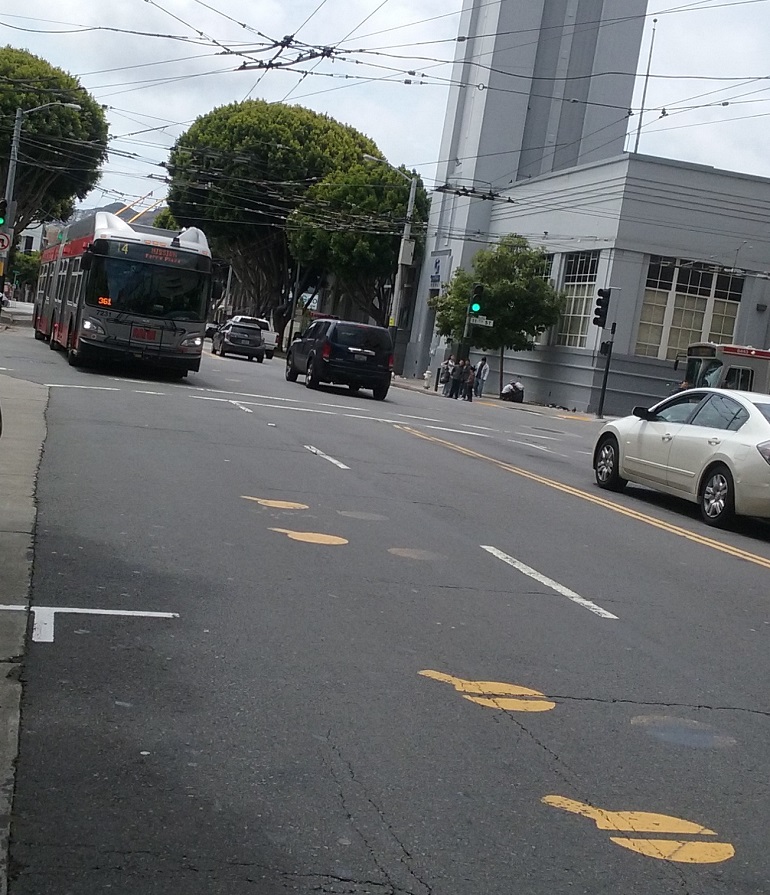 An electric trolley bus approaches a series of four yellow dot markings on the road pavement.