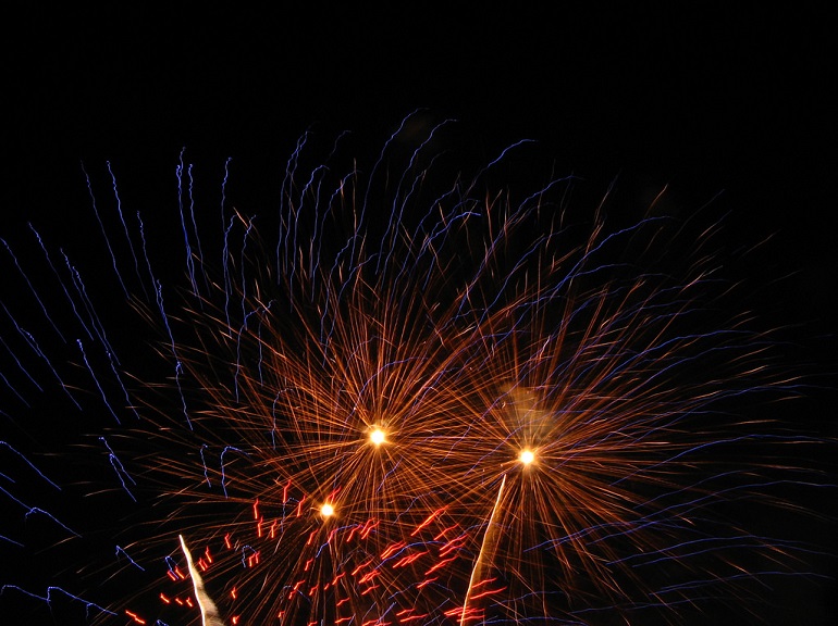 Colorful fireworks explode against a pitch black night sky.