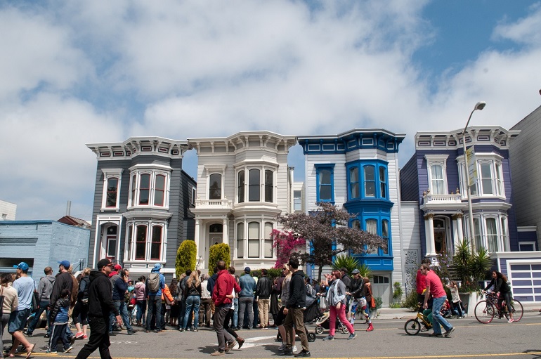 People walk and bike on Valencia Street in front of four Edwardian homes.