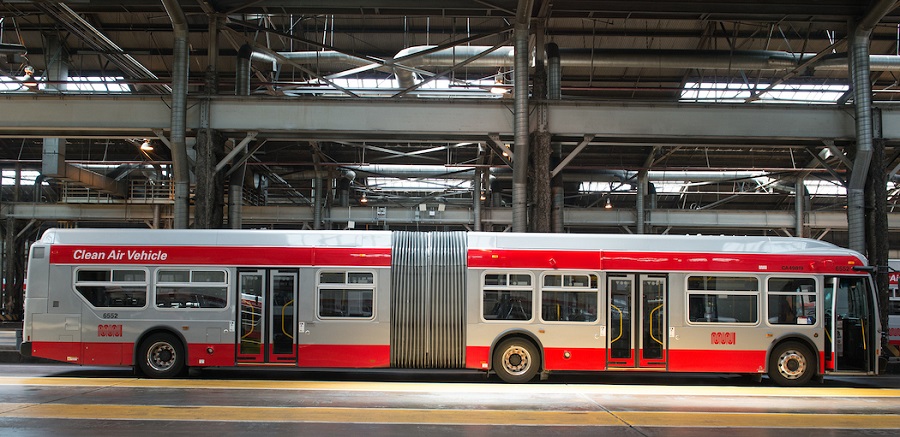 A 60-foot Muni bus parked in a garage with its front door open.