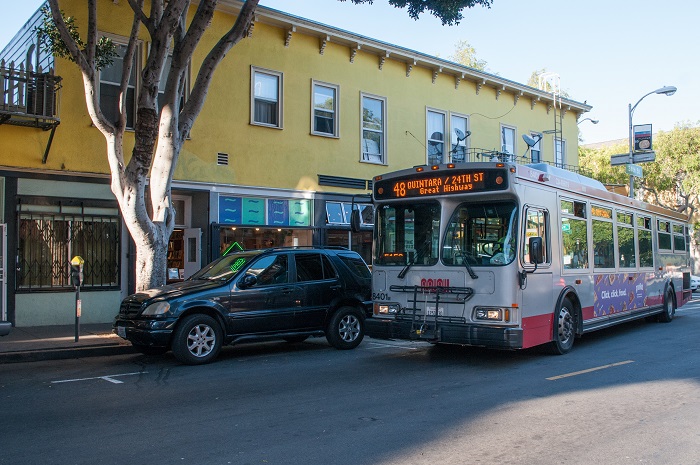 Outbound 48 Quintara-24th Street bus driving past a yellow building in the afternoon.