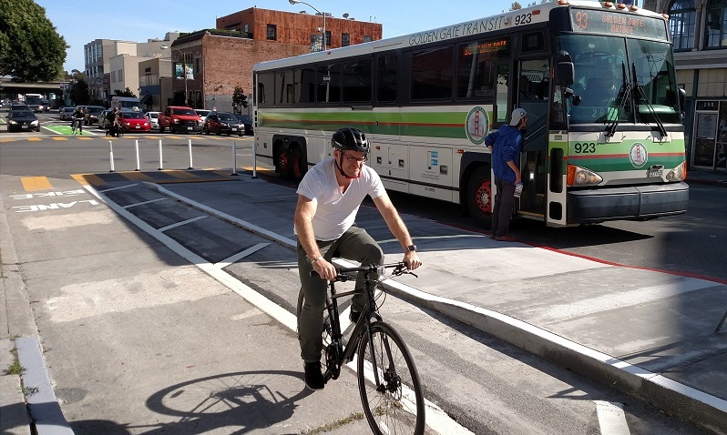 Man biking in a parking-protected bike lane and transit boarding island on 7th Street.