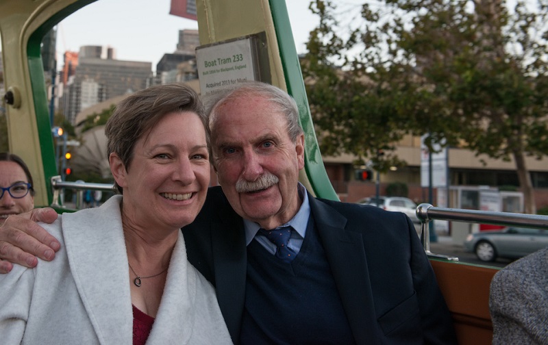 Man and woman sit beside each other on an open-air streetcar.