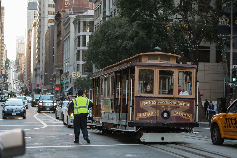 California Cable Car being guided by a parking control officer in traffic.