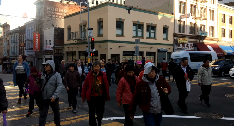 People walk diagonally across the intersection of Clay and Kearny streets.