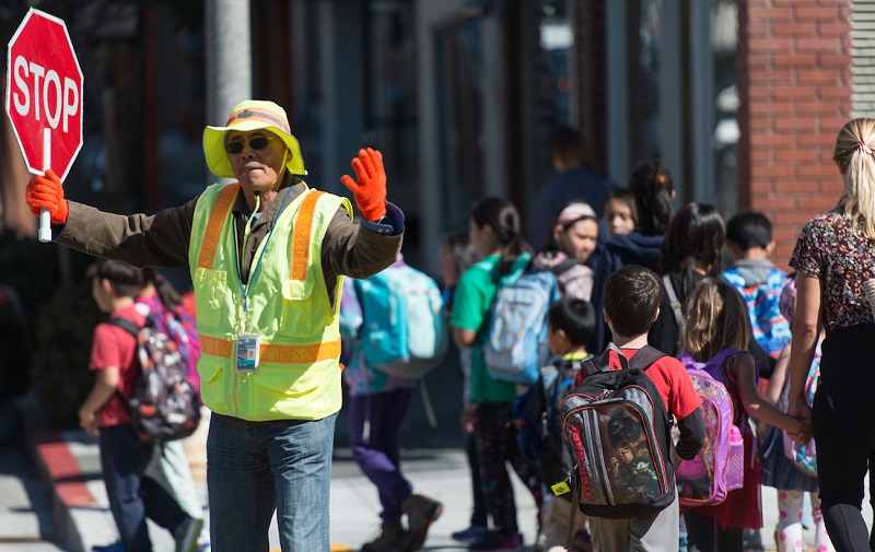 Crossing guard holding stop sign as students and parents cross the street.