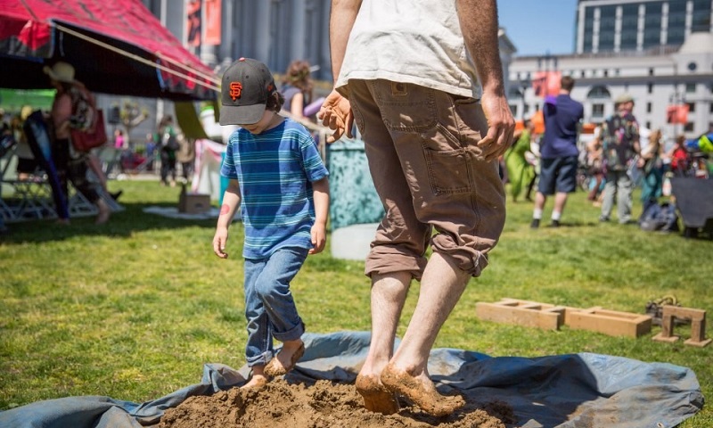 A man and child walk barefoot in mud at the Earth Day Festival in Civic Center Plaza.