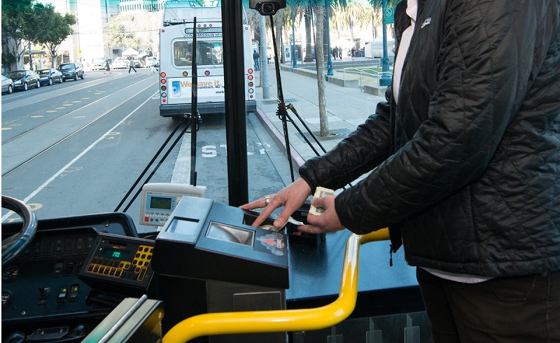 Man on a Muni bus feeding cash bills into a farebox.