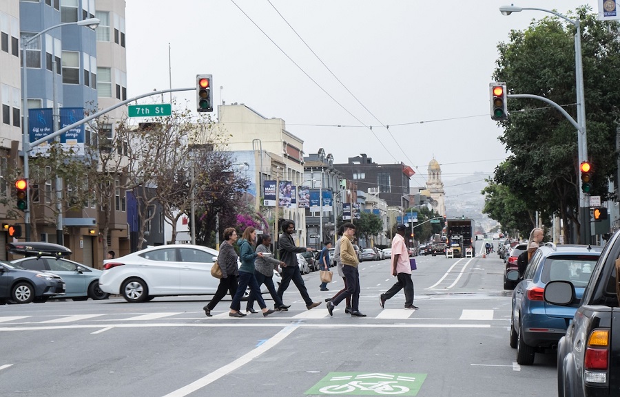 People and car traffic cross Howard Street at 7th Street. Howard has three traffic lanes, a bike lane and two parking lanes.