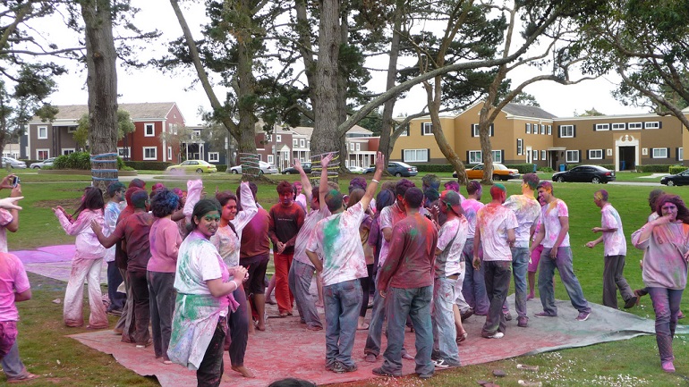 Dozens of people covers in colorful dye in the middle of a park surrounded by trees