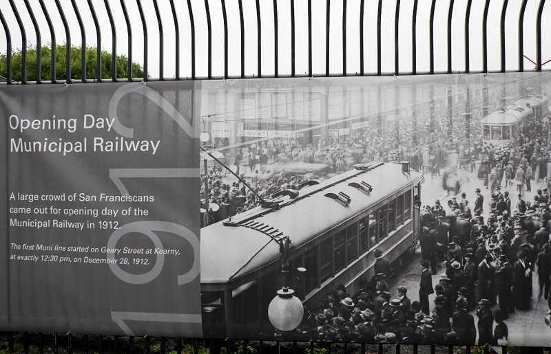 A section of the timeline banner on the Kirkland yard fence titled, "Opening Day - Municipal Railway," featuring a photo from 1912 showing crowds around streetcars.