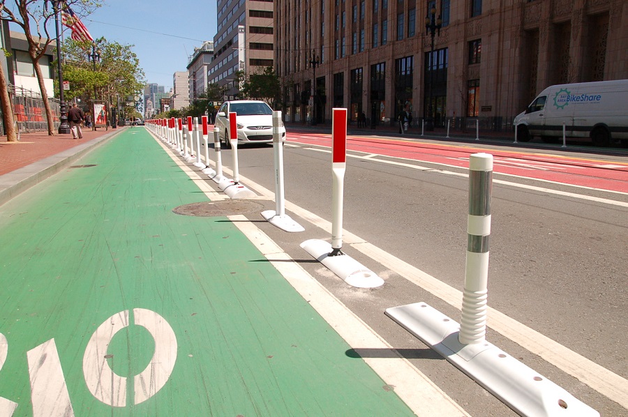 Market Street bike lane with plastic safe-hit posts of different heights and colors, that feature a raised plastic curb at their base.