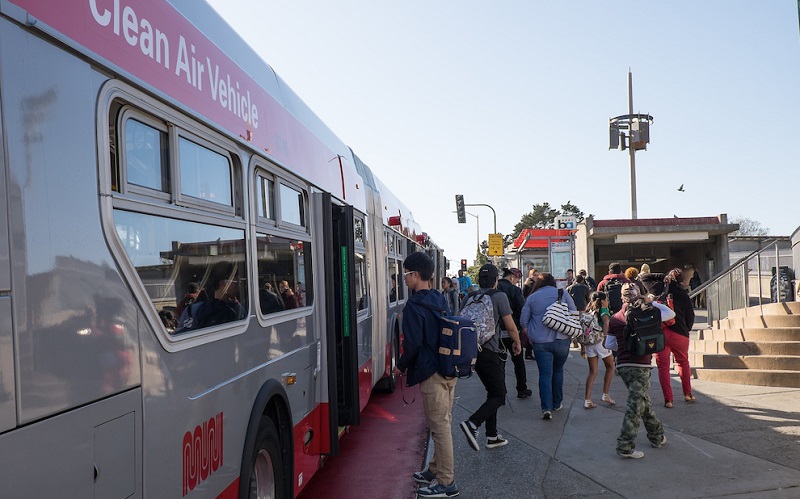 People board a Muni bus in front of Balboa Park Station.