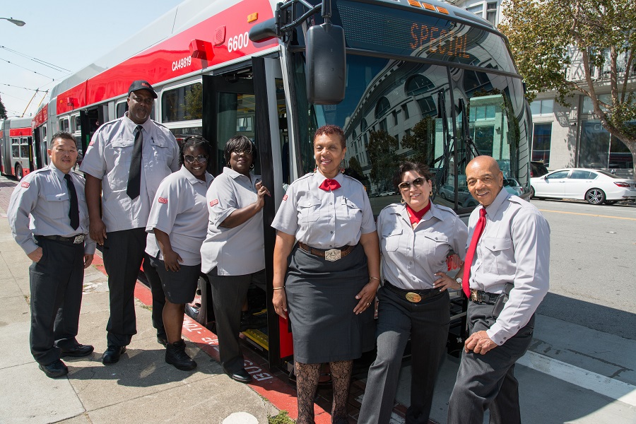 Muni operators pose in their new uniforms in front of a parked Muni bus.