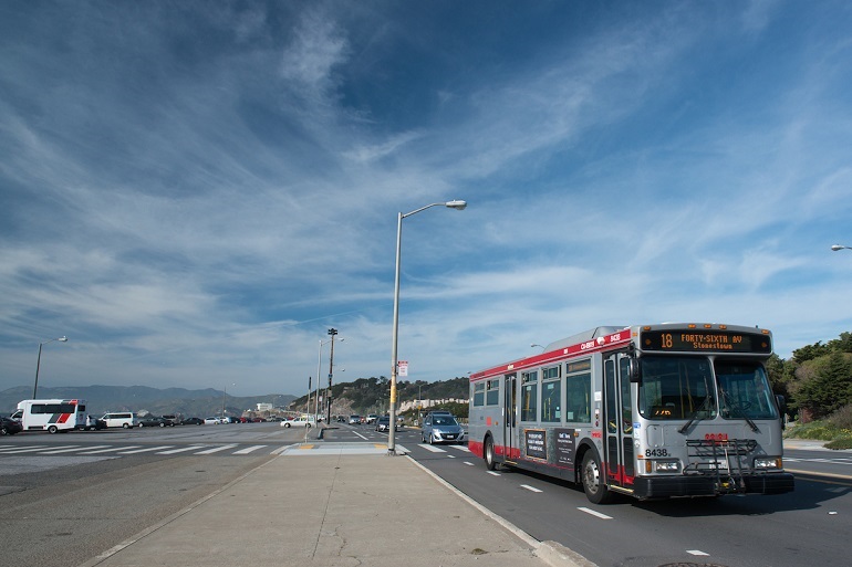 Muni bus travelling on the Great Highway under a bright blue sky.