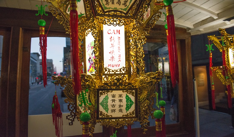 Photo of a Chinese lantern with "CAM," "Happy New Year" and "Muni" written in English next to Chinese characters, on the inside of a motorized cable car.