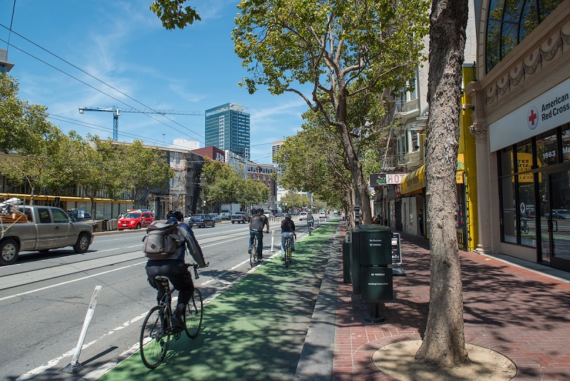 Bike lane at road-level, with green-painted pavement and plastic posts separating it from vehicle traffic.