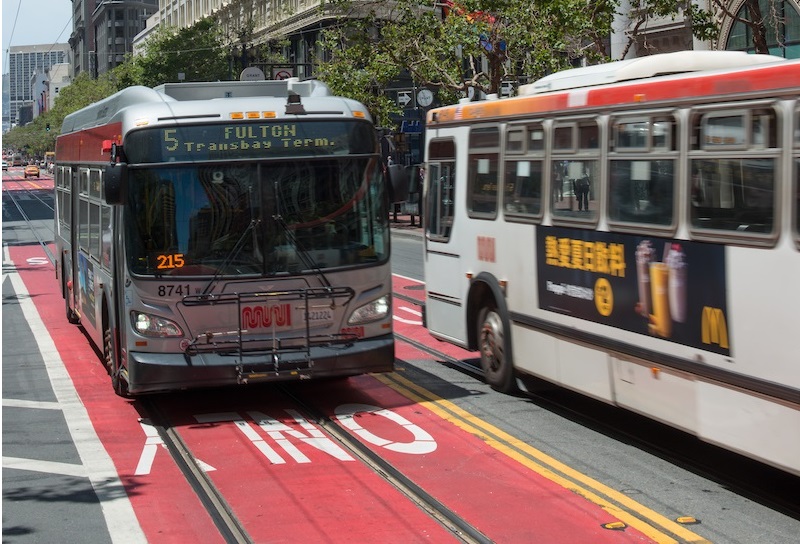 Muni buses drive down red-colored transit-only lanes on Market Street.