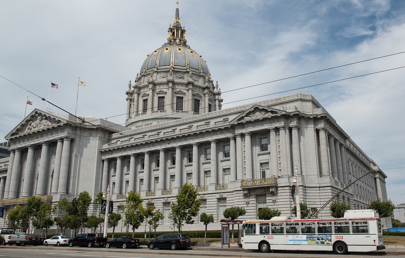 San Francisco City Hall viewed from Van Ness Avenue, with cars and a Muni trolley bus on the street.