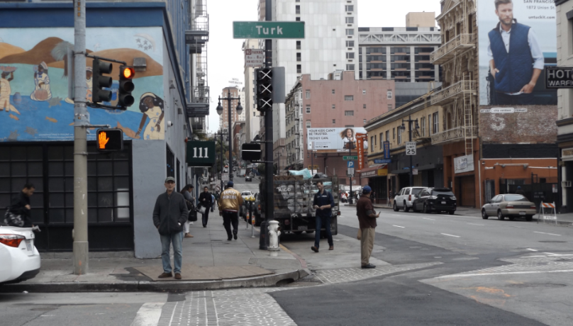 Pedstrians cross downtown streets with the "Turk" street sign above them.