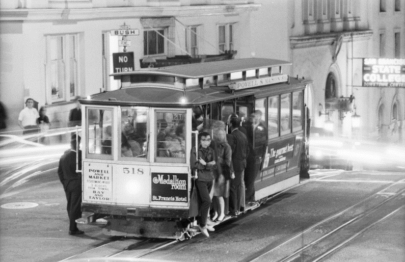 A 1968 photo of people riding a cable car at night as it stops at Powell and Bush streets.