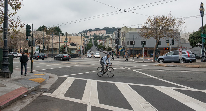 Daytime view looking west on 14th Street at its intersection with Market and Church streets with people walking, driving and a man bicycling.