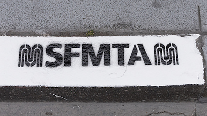 White painted curb with black stencil that reads "SFMTA"