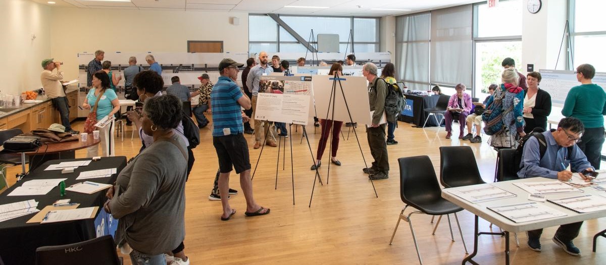 Image of Geary Rapid Project Open House with members of the public interacting with project staff at different stations. 