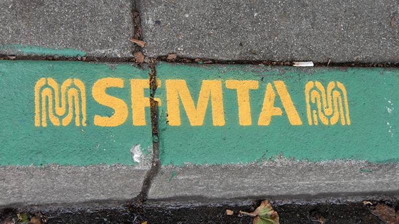 Painted green curb with stencil that says "SFMTA"