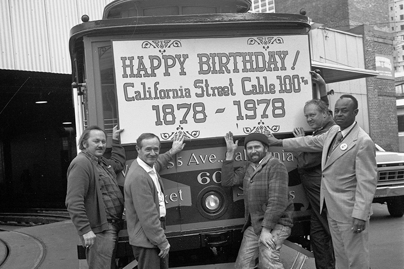 shop personnel holding sign up against cable car 